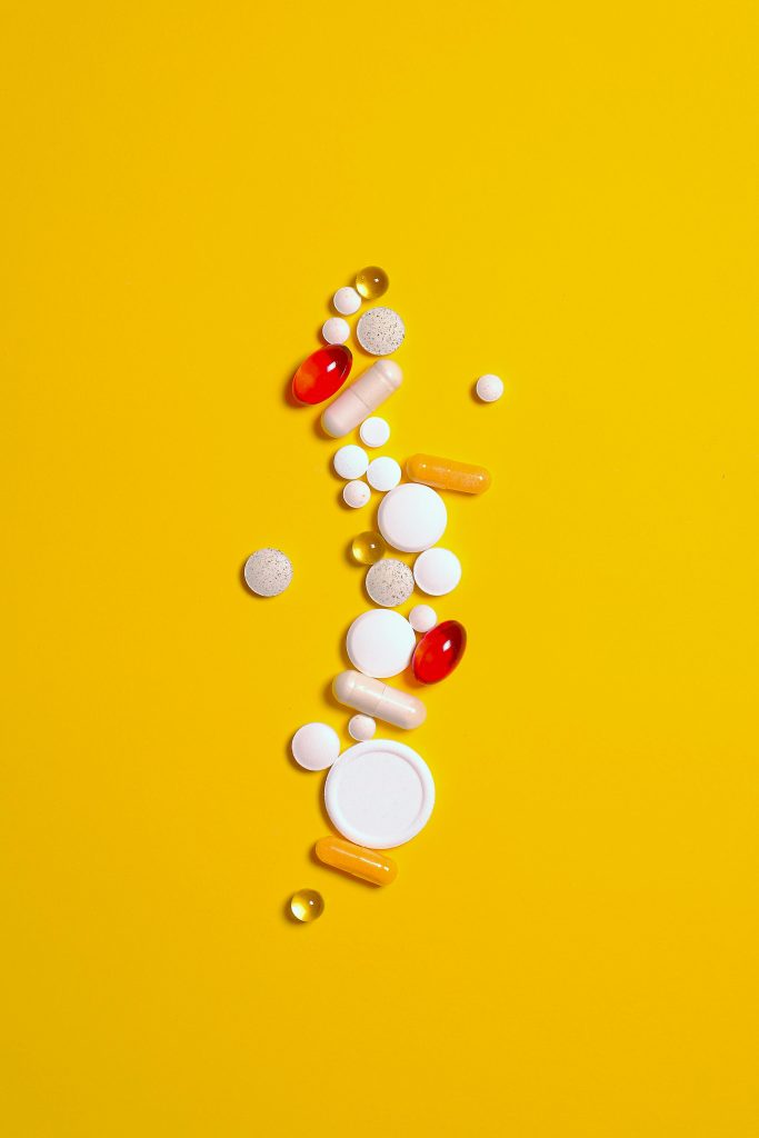 Assorted pills in vibrant colors on a striking yellow background, representing healthcare and medicine.